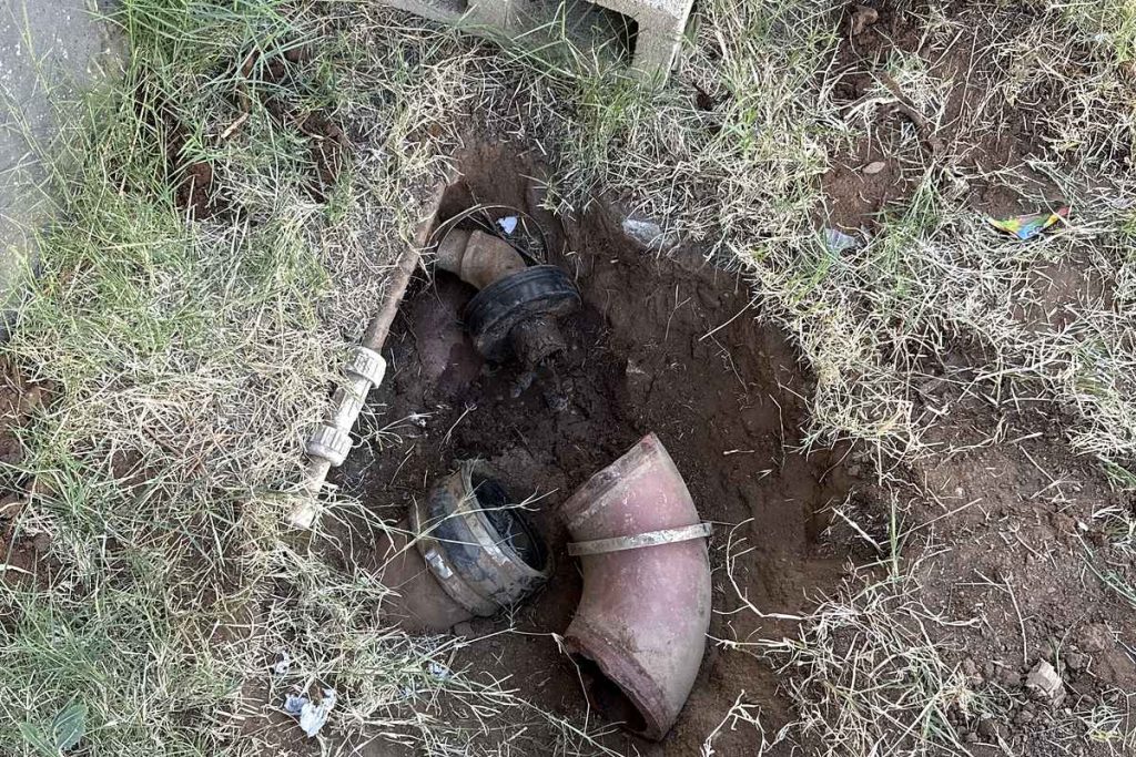 Old cast iron sewer elbow exposed in a yard excavation