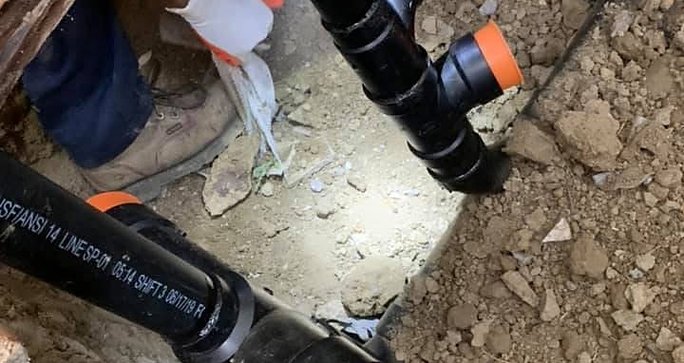 Technician setting new ABS sewer pipe in a trench
