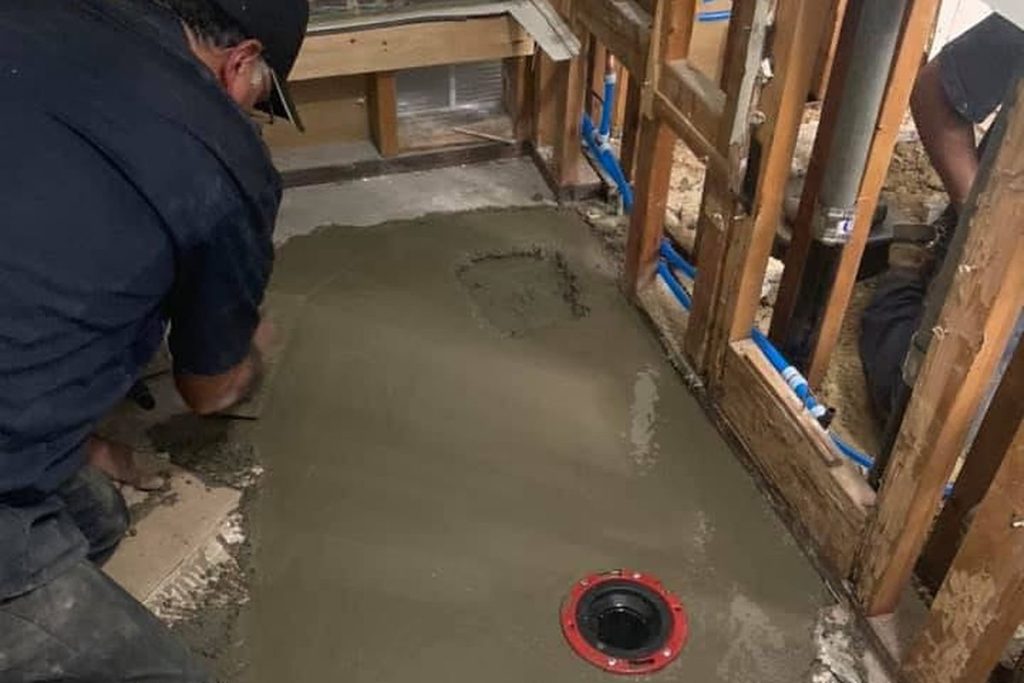 Technician finishing concrete around a new closet flange