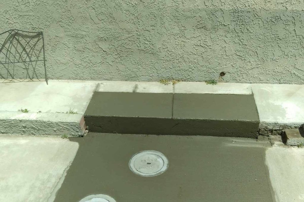 Cleanouts set into a fresh concrete patch at a stucco wall