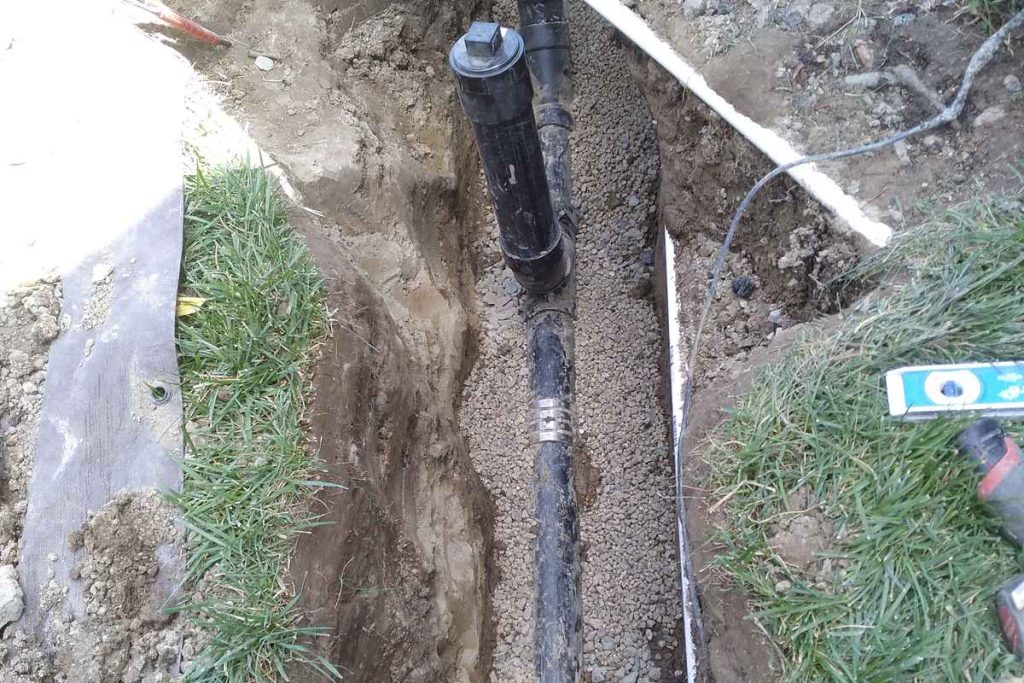 New sewer pipe bedded in a trench across a lawn